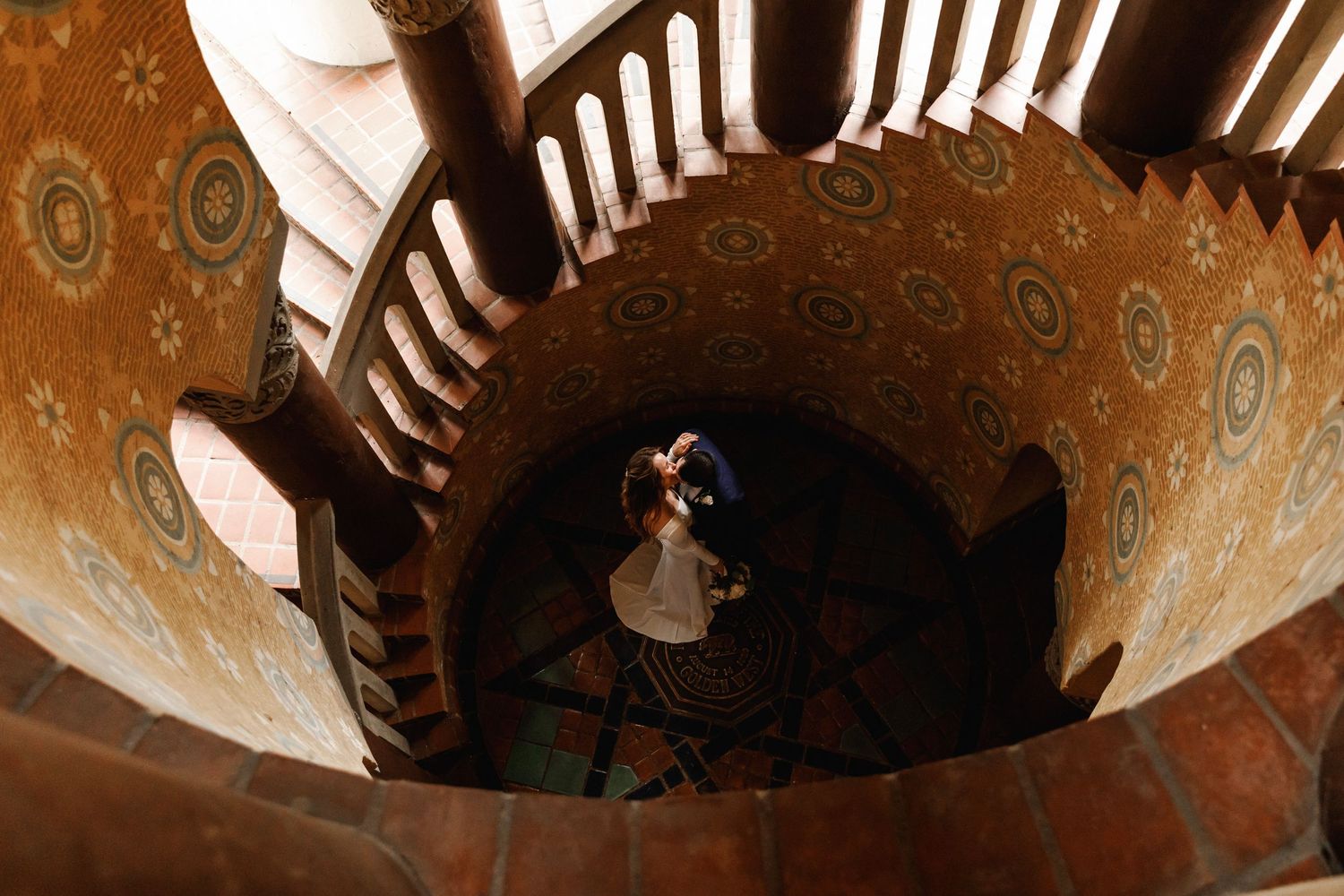 Aerial view of a bride and groom embracing at the center of a stunning ornate spiral staircase.