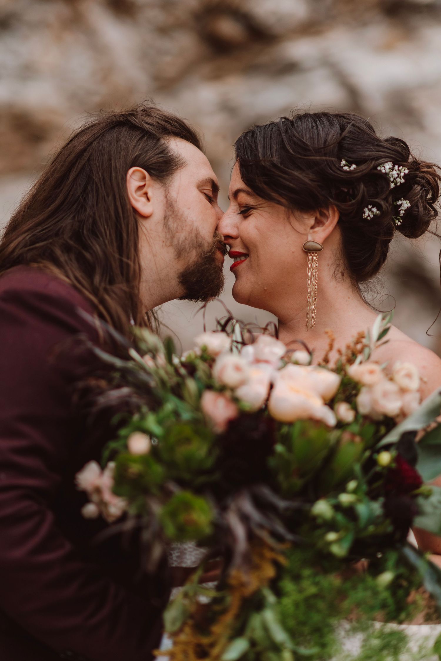 Couple shares an intimate moment nose-to-nose with a lush floral bouquet of roses in the foreground.