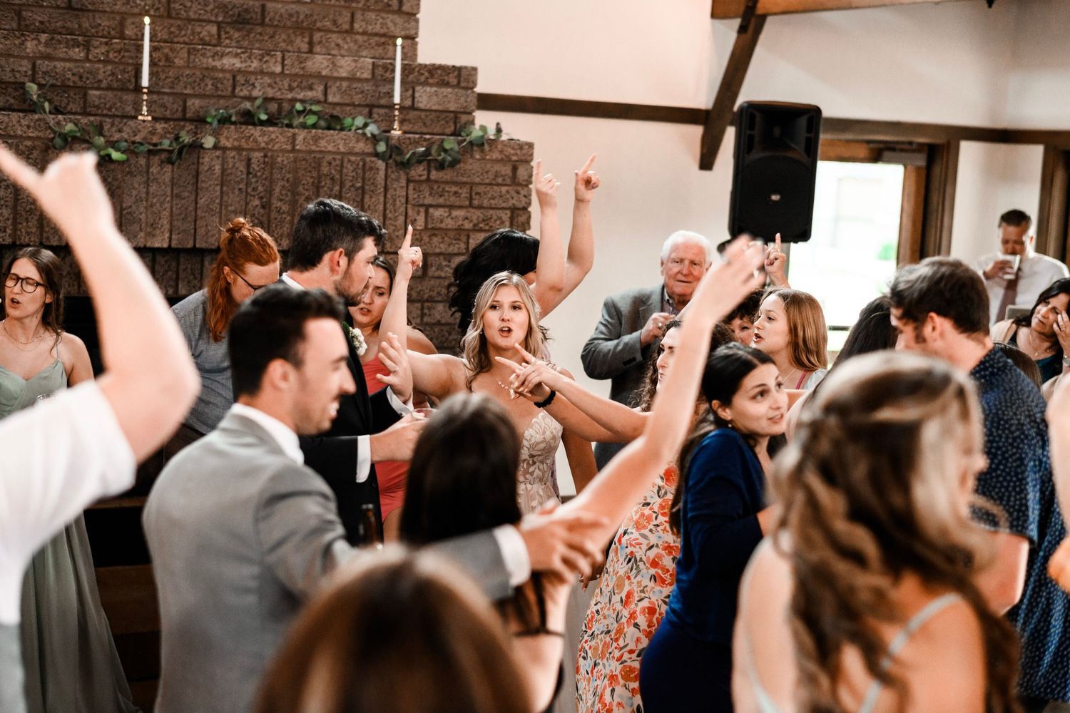 Lively wedding reception dance floor filled with guests celebrating with hands raised.