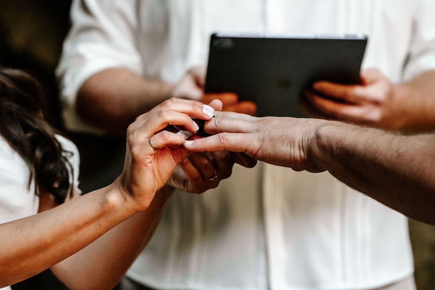 Close-up of couple exchanging rings during wedding ceremony while officiant holds tablet.