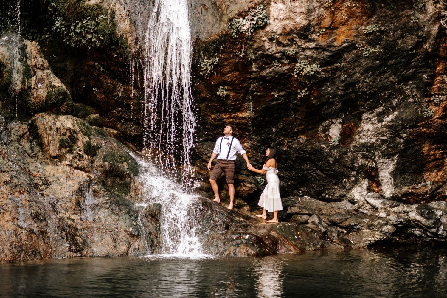 Couple holding hands near stunning waterfall during romantic outdoor elopement session.