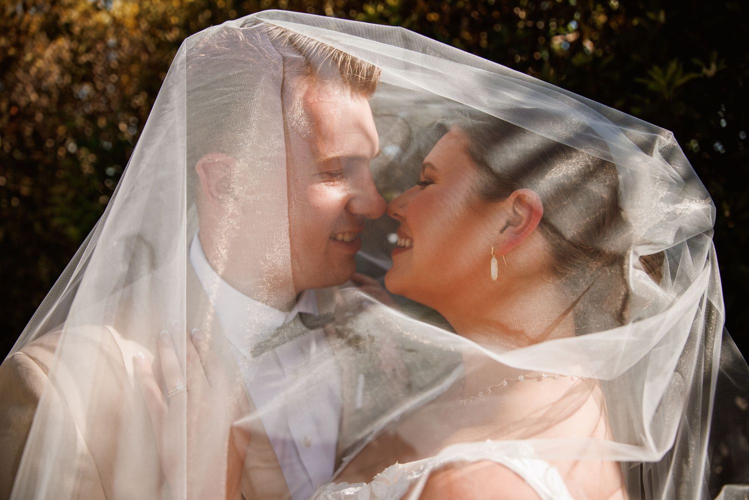 Bride and groom sharing a kiss under a sheer wedding veil outdoors.