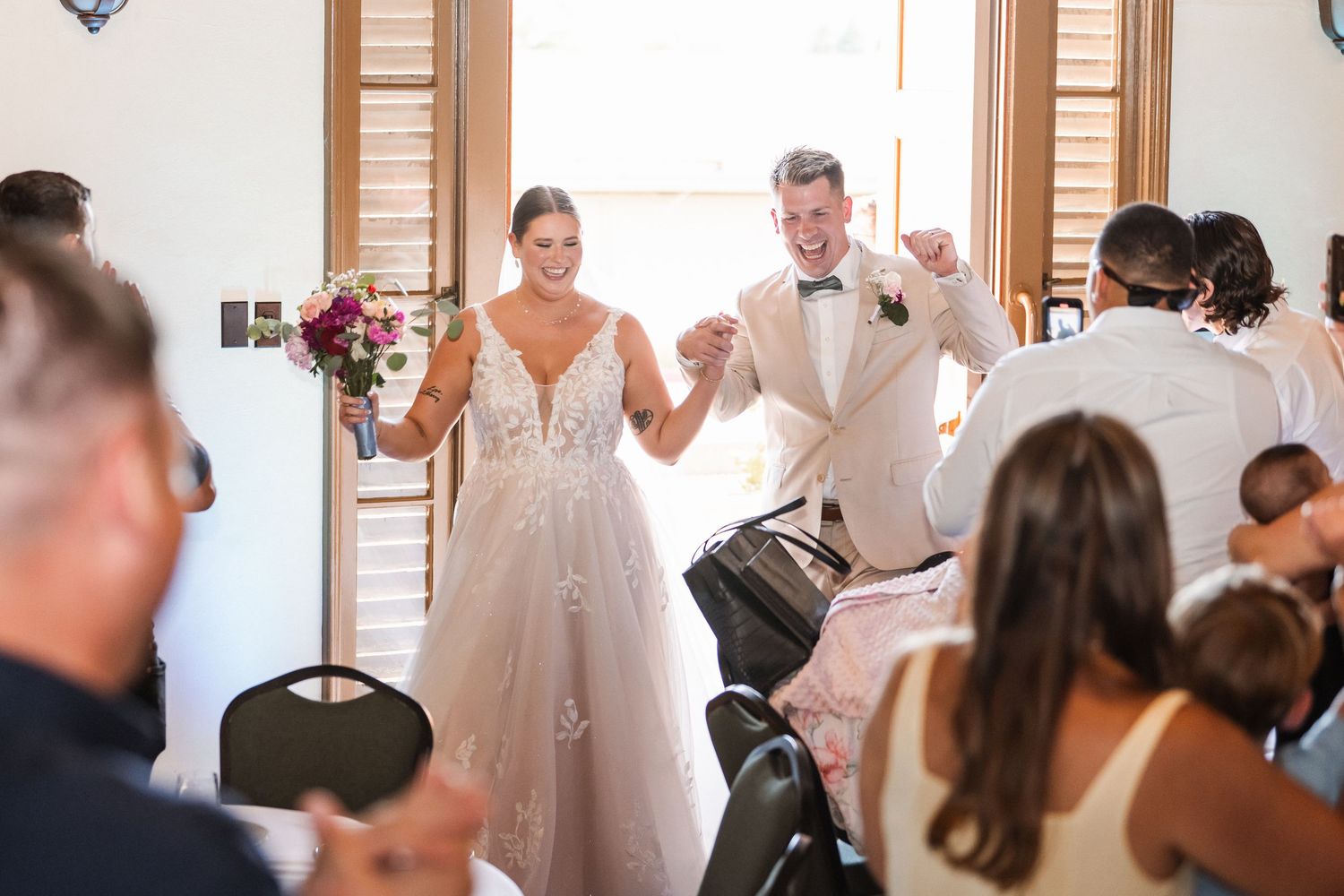 Joyful bride and groom entering wedding reception to applause from seated guests.