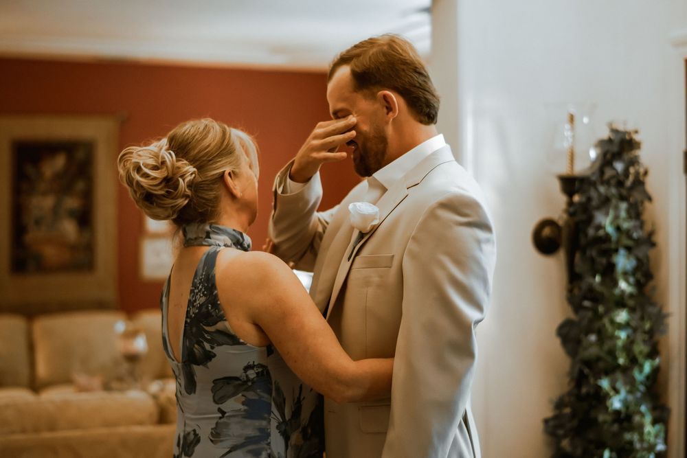 A couple shares an emotional moment indoors, with the woman tenderly touching the man's face as he wipes away tears.