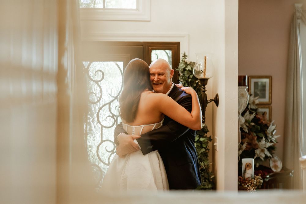 Bride and father sharing an emotional first look hug in a warmly decorated home entryway on wedding day.