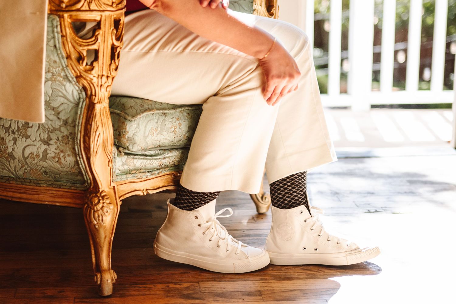 Person sitting on ornate gold chair wearing white Converse sneakers and fishnet socks with cream trousers.