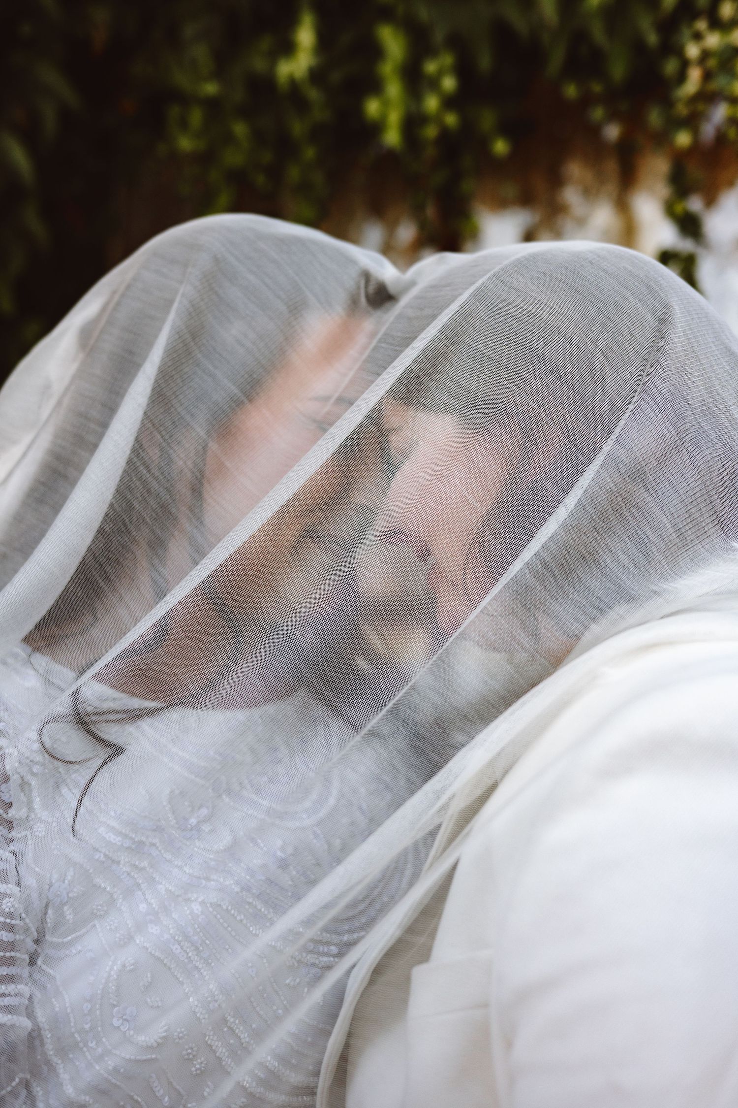 Romantic couple sharing an intimate moment under a sheer bridal veil outdoors.