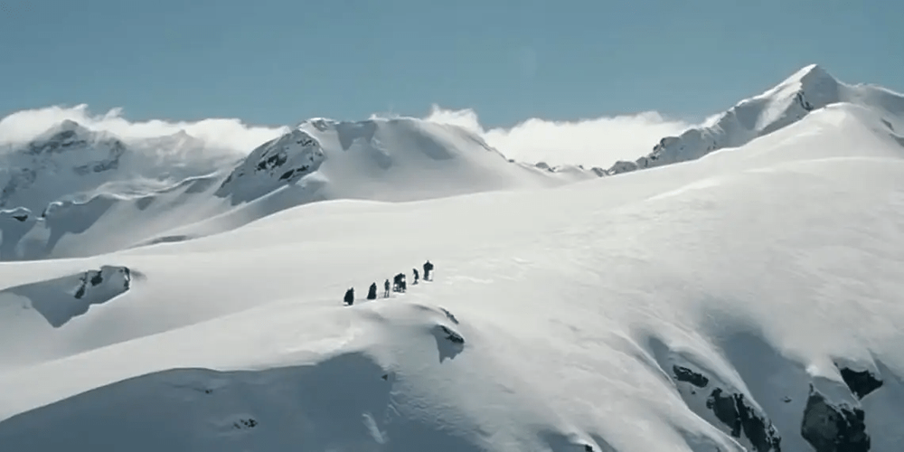 Small group of mountaineers trekking across snowy alpine terrain.