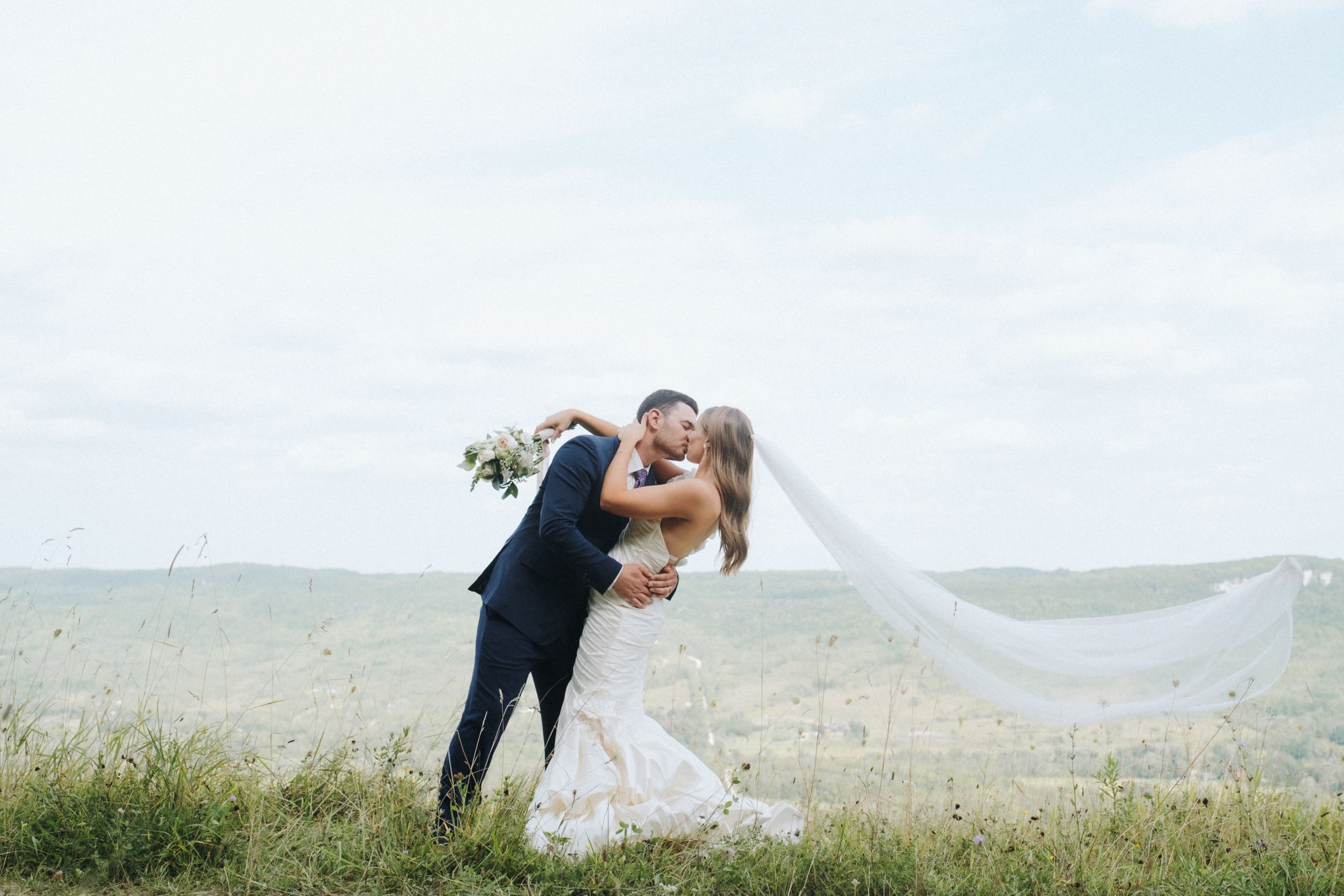 A romantic moment between newlyweds on a scenic hilltop with flowing veil.