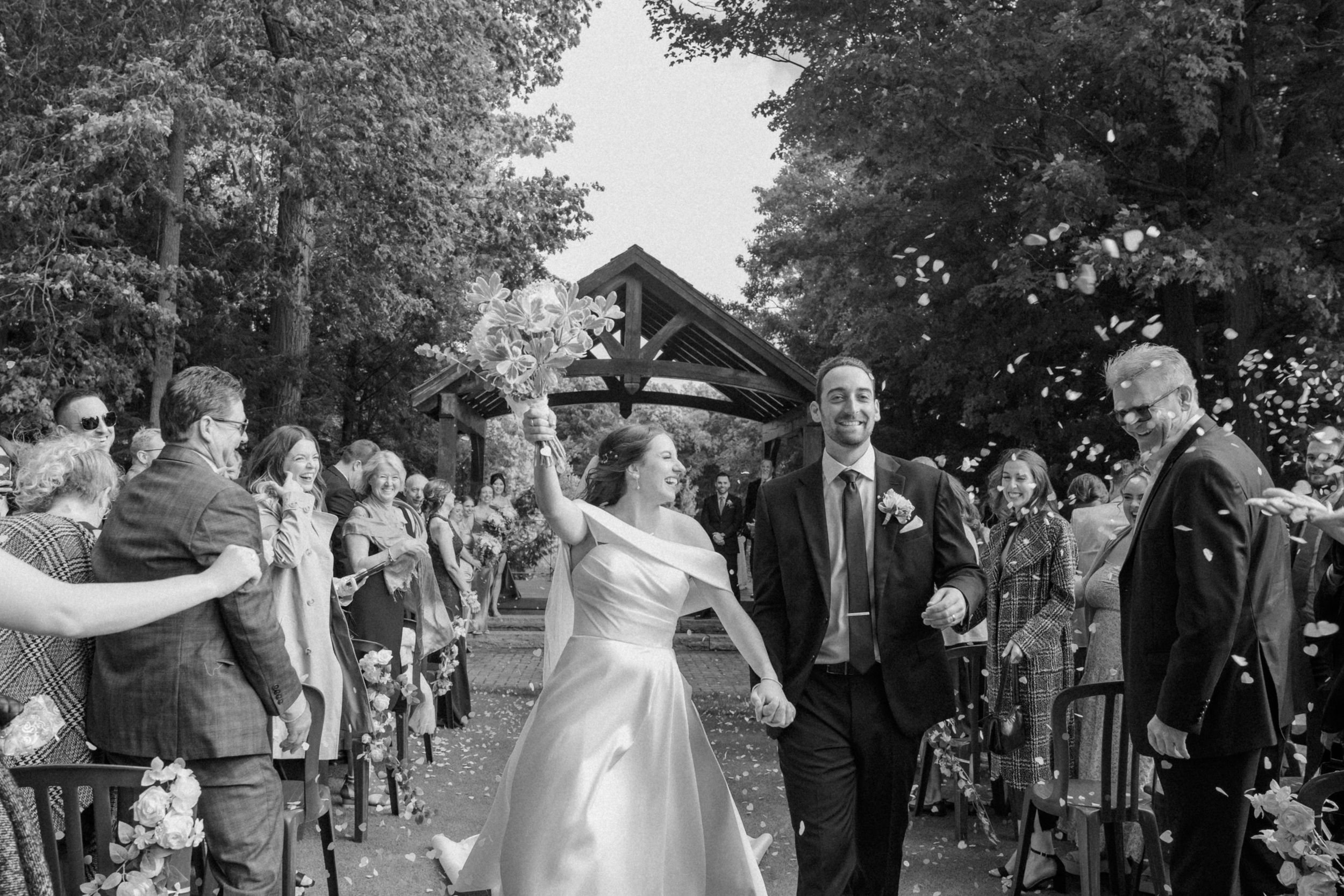 Wedding celebration with guests cheering for newlyweds outside rustic wooden chapel.