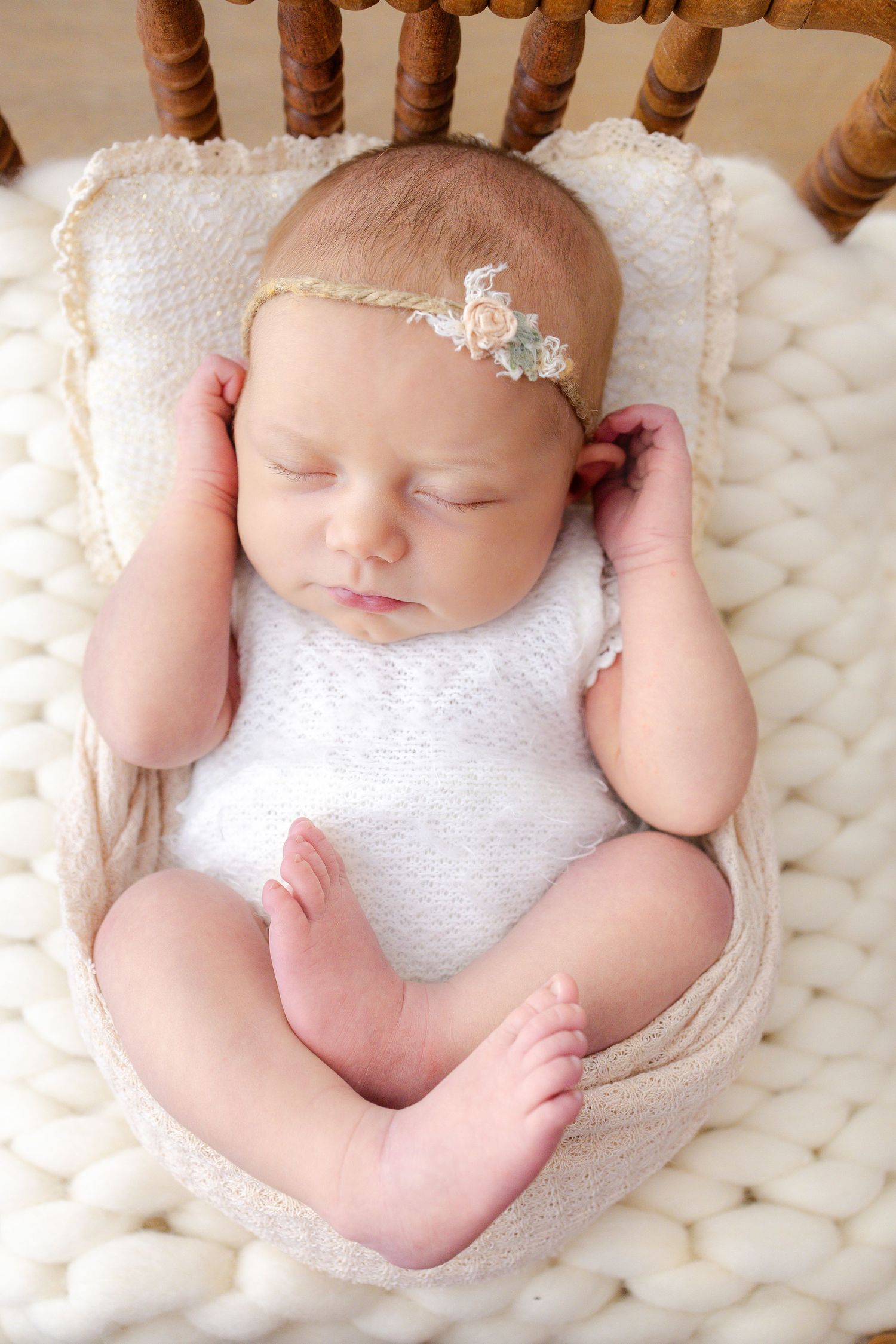 Sleeping newborn in purple outfit nestled in knit wrap on white fluffy blanket with matching bow headband.