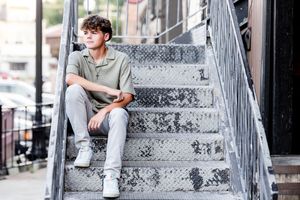 Person sitting on concrete steps wearing casual streetwear and white sneakers in urban setting.