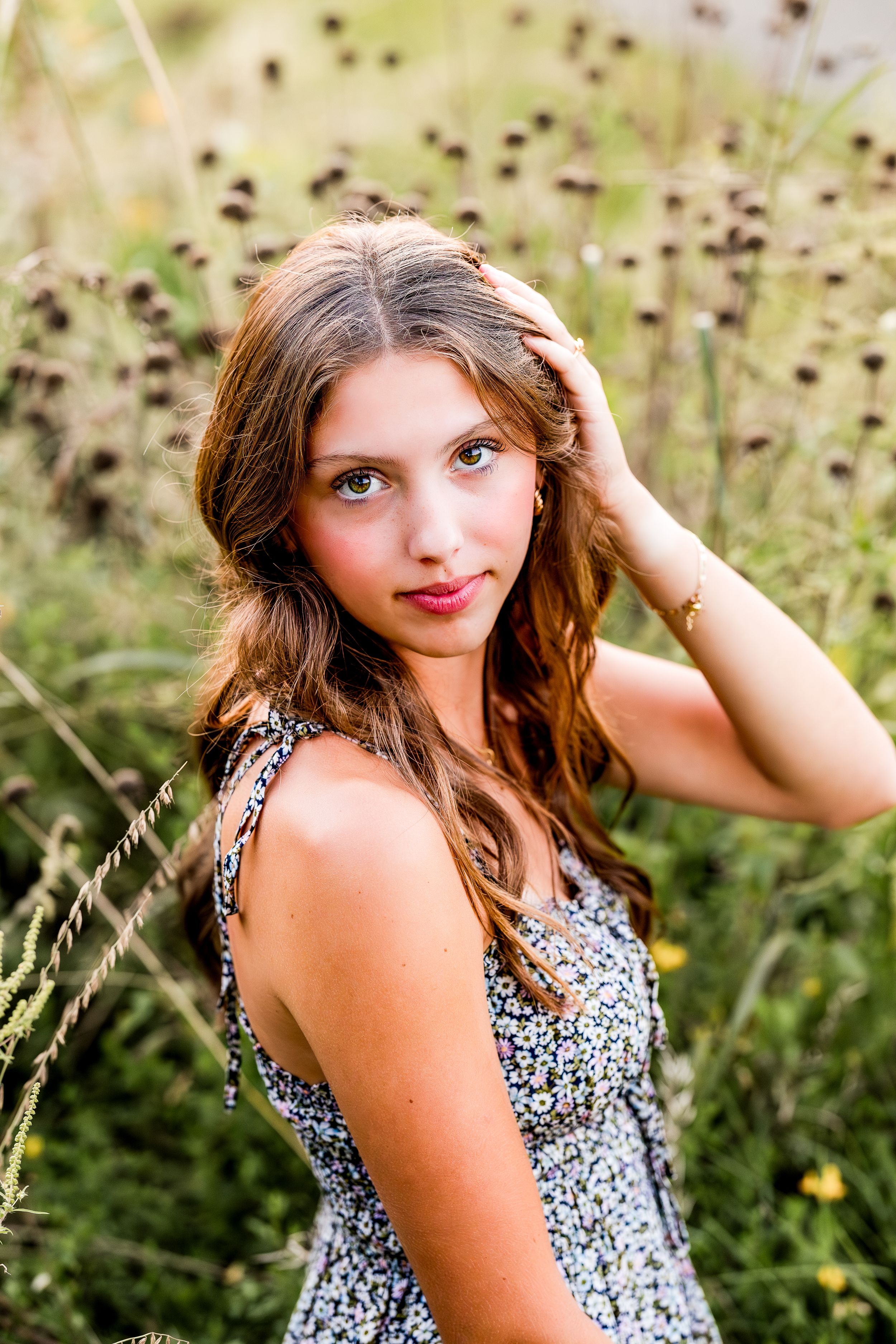A person in a floral print dress poses outdoors among wildflowers and natural scenery in a series of portraits.