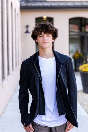 Young person in a navy blazer and white t-shirt poses in front of a light-colored building exterior.