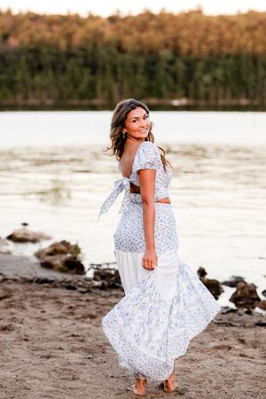A young girl in a white polka dot dress twirls and plays on a sandy beach at sunset.