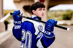 High school hockey player in blue and white jersey number 30 poses with stick over shoulders outdoors.