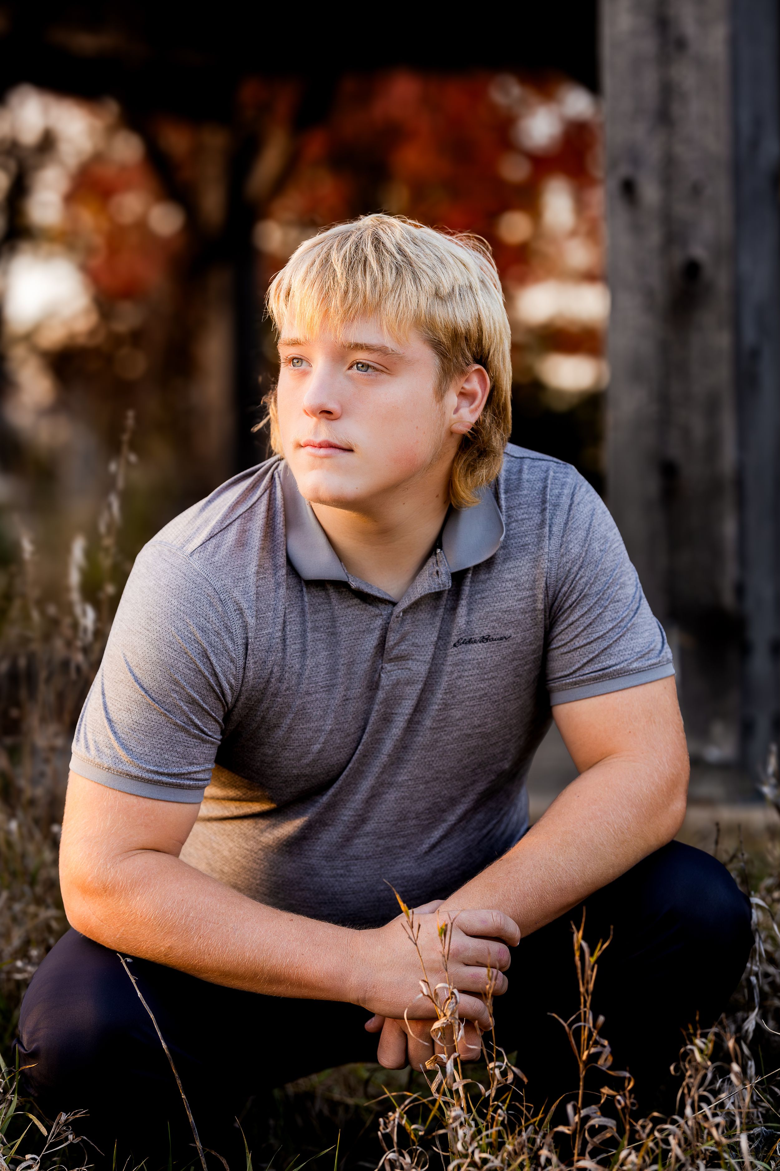 A person in a gray polo shirt poses thoughtfully in a natural outdoor setting with warm autumn lighting.