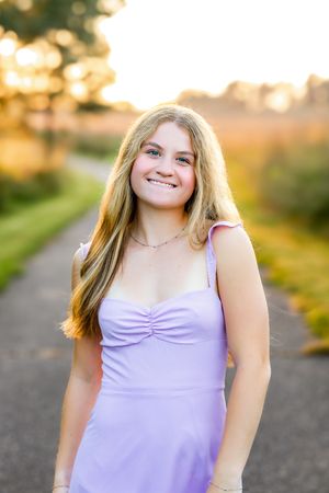 A person in a lavender dress poses outdoors during golden hour sunset lighting.