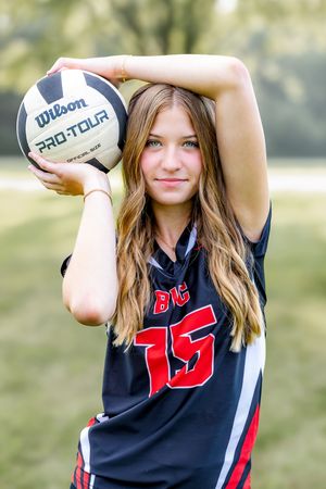 Football player in black and red jersey poses with ball in outdoor photoshoot series.