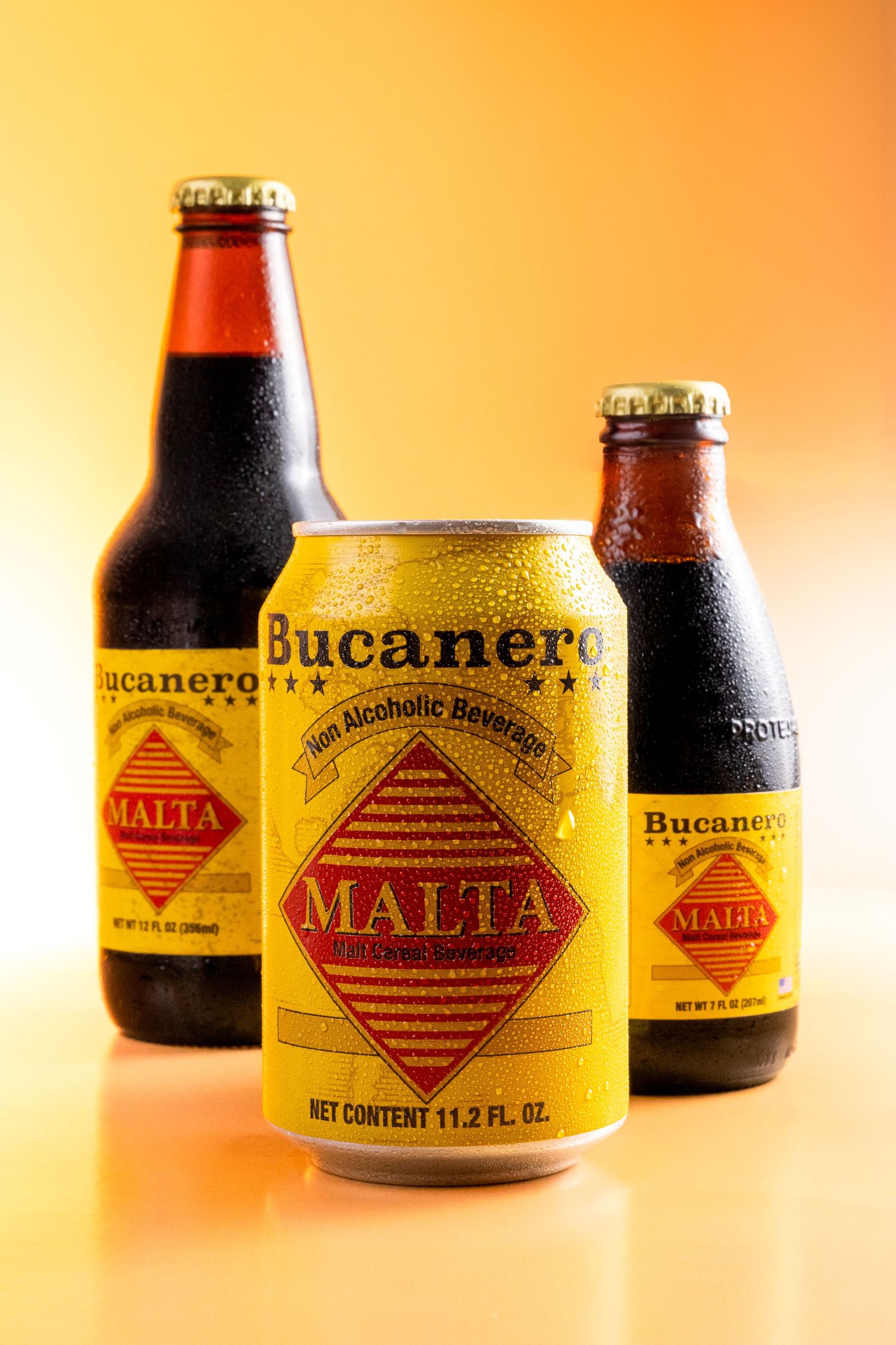 Multiple vintage Bucanero Malta soft drink bottles arranged on an orange background with warm lighting.