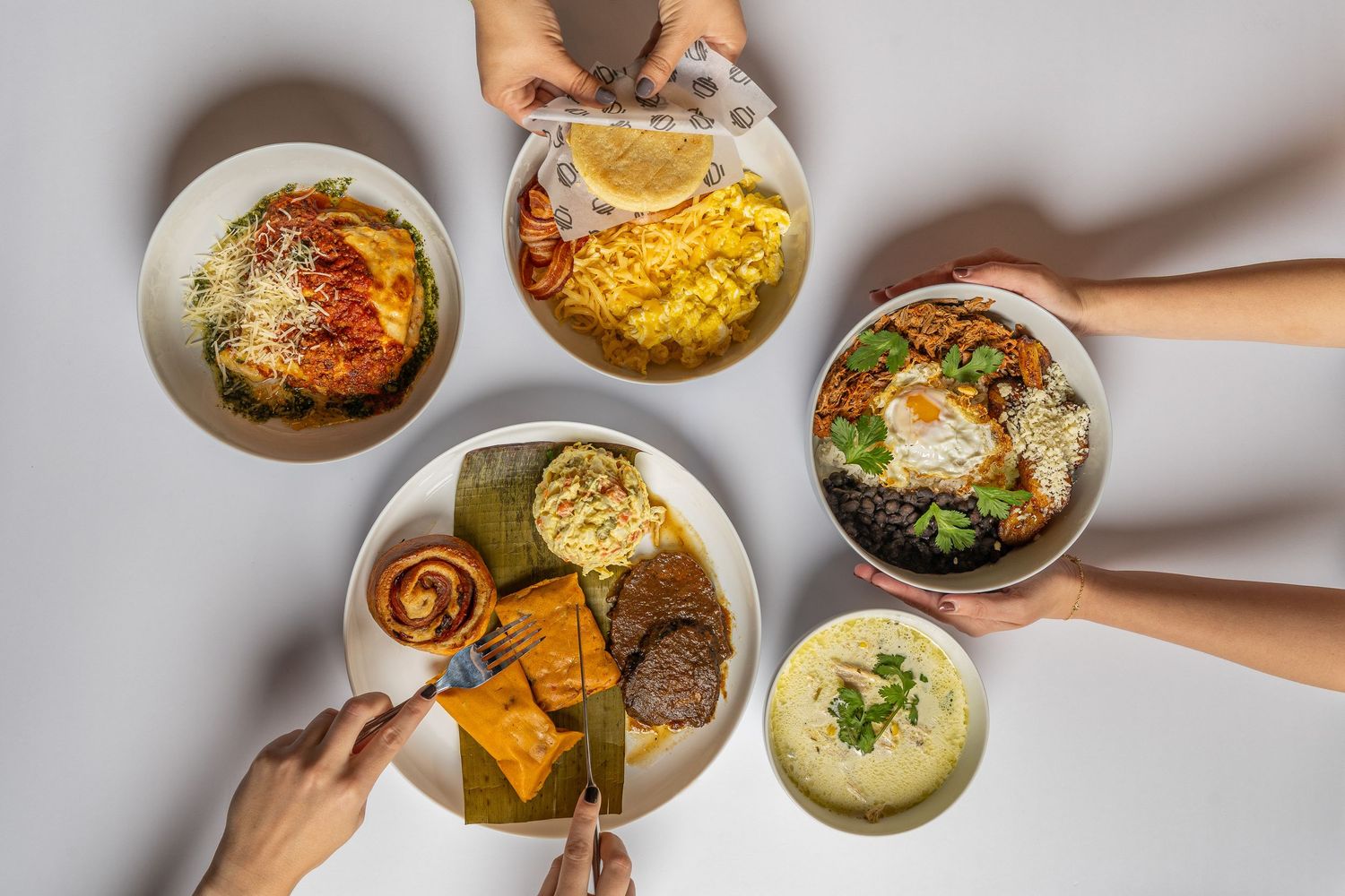Overhead view of colorful food bowls and plates shared by friends, featuring rice, eggs, and vibrant toppings.
