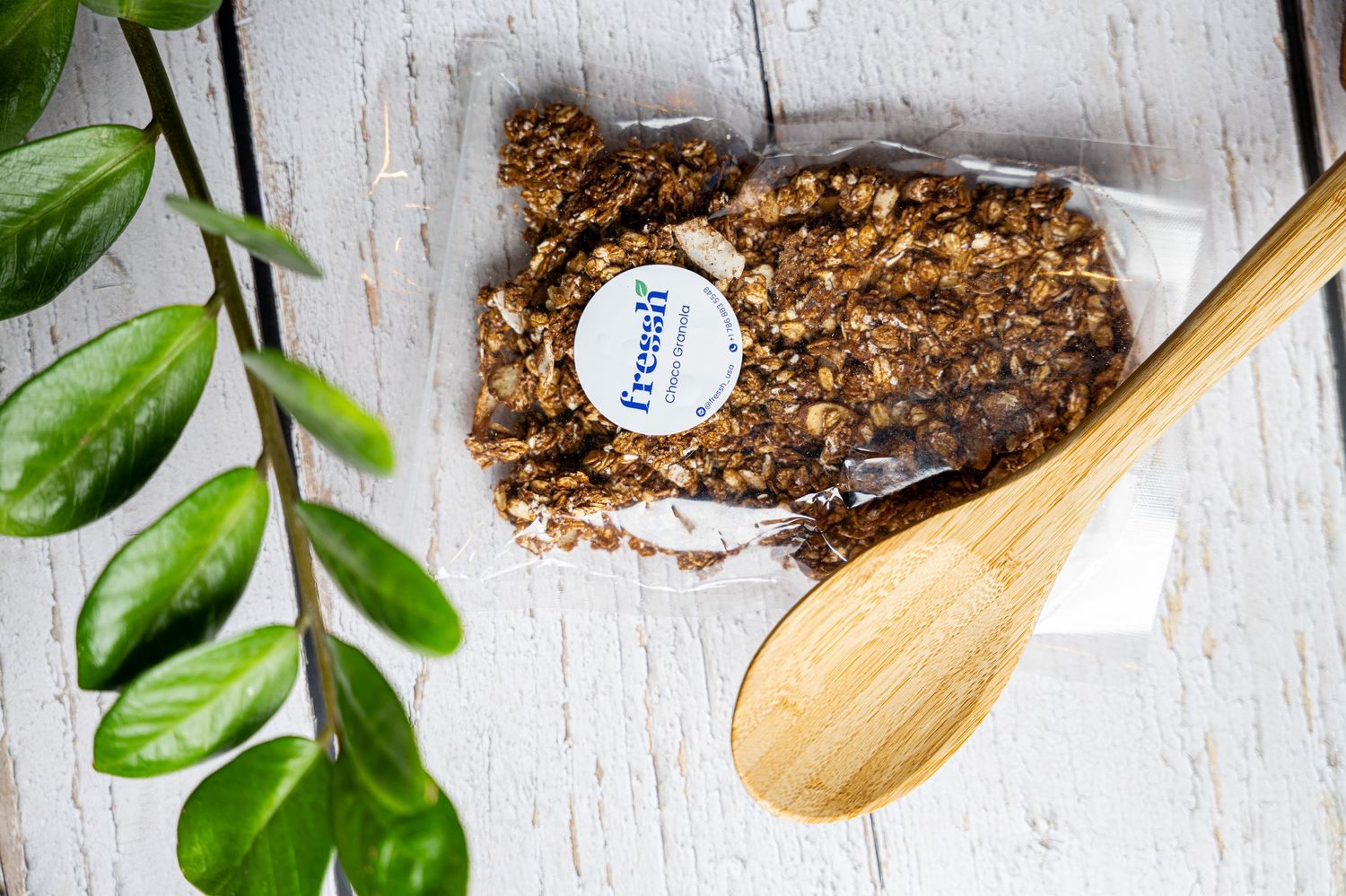 Wooden spoon scooping ground coffee beans with green leaves against a white wooden background.