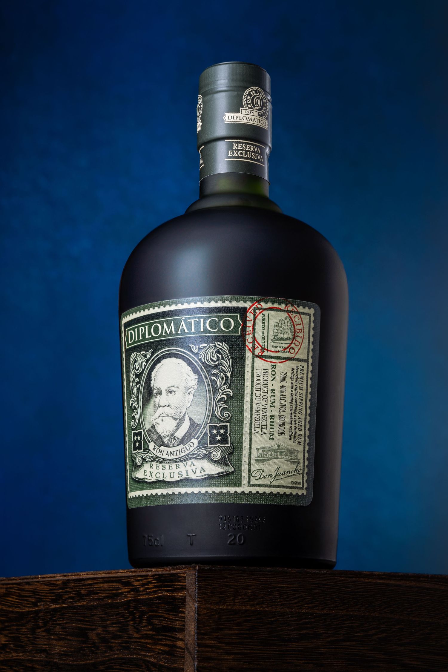 Bottle of Diplomatico rum with black frosted glass and vintage-style label photographed against dark blue background.
