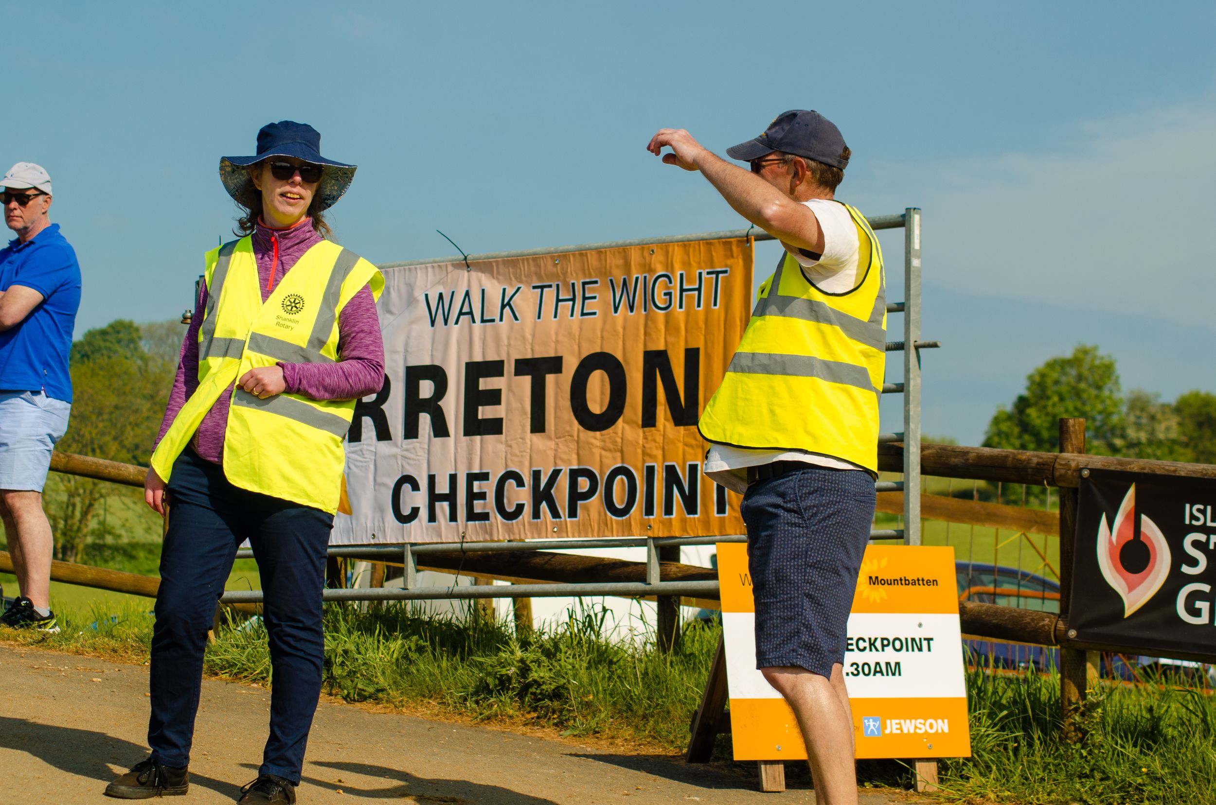 Volunteers in high-vis vests stand at Breton checkpoint sign during outdoor event.