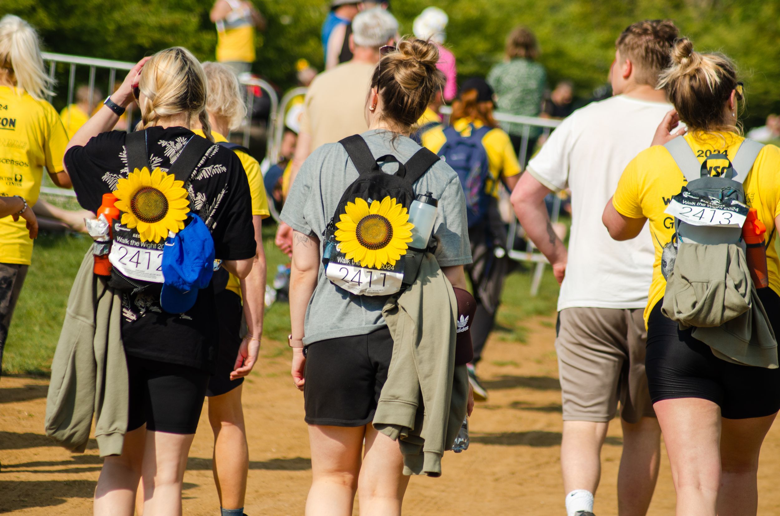 Hikers with sunflower-decorated backpacks walking along trail during organized event.