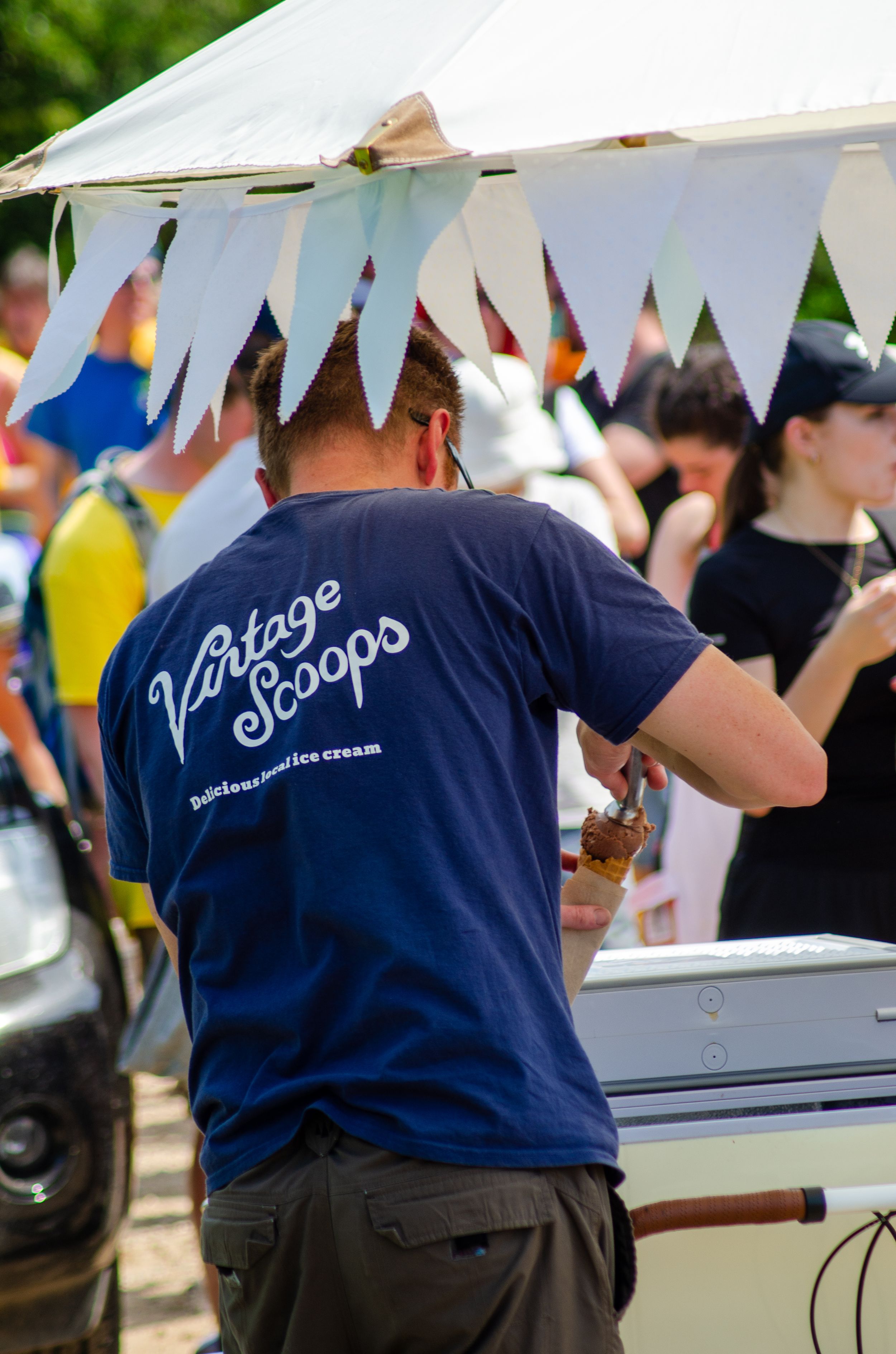 Vintage Scoops ice cream vendor stands under white tent with banner decorations.