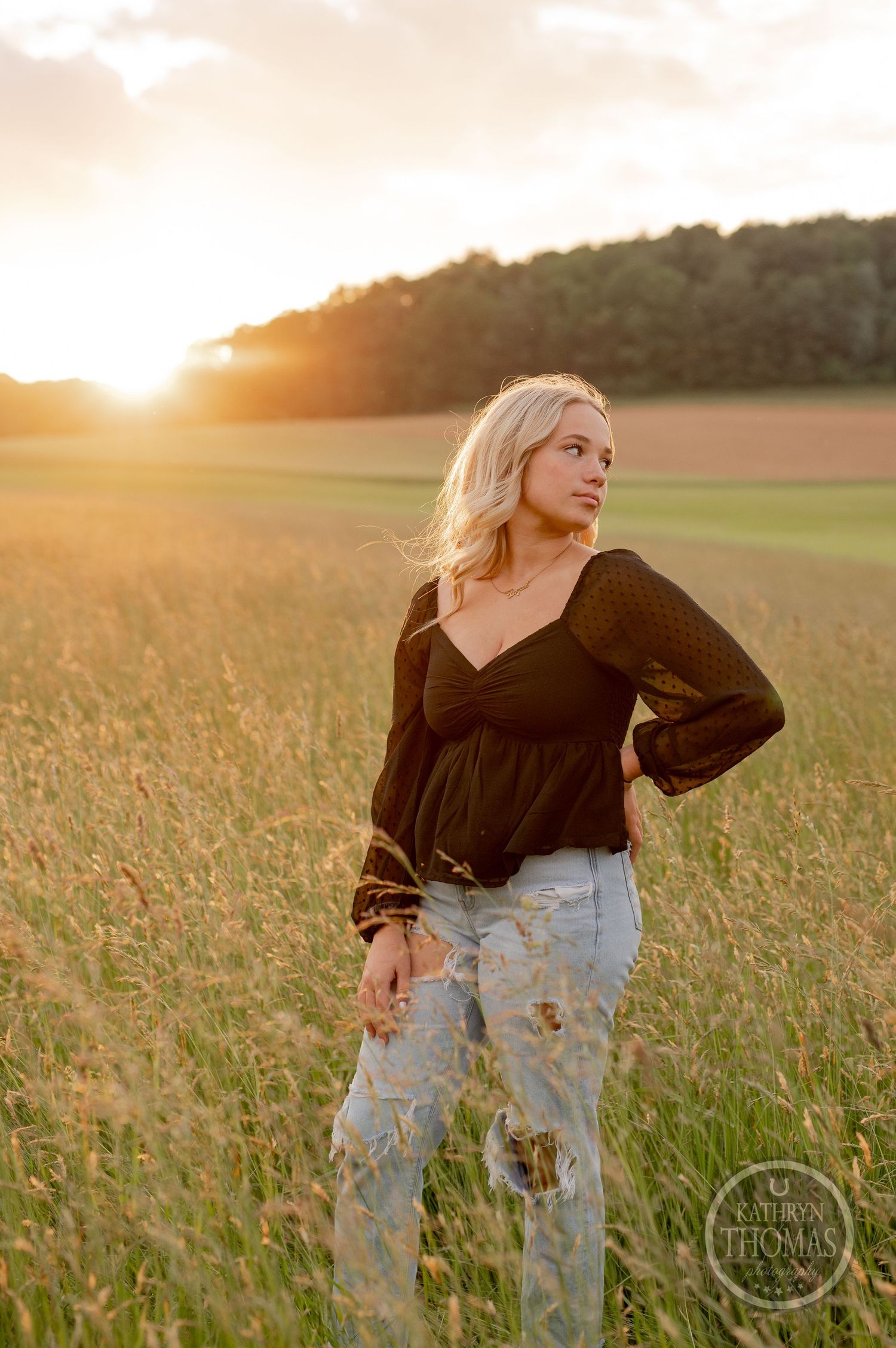 Golden hour portrait in a field wearing a black sweater and distressed jeans.