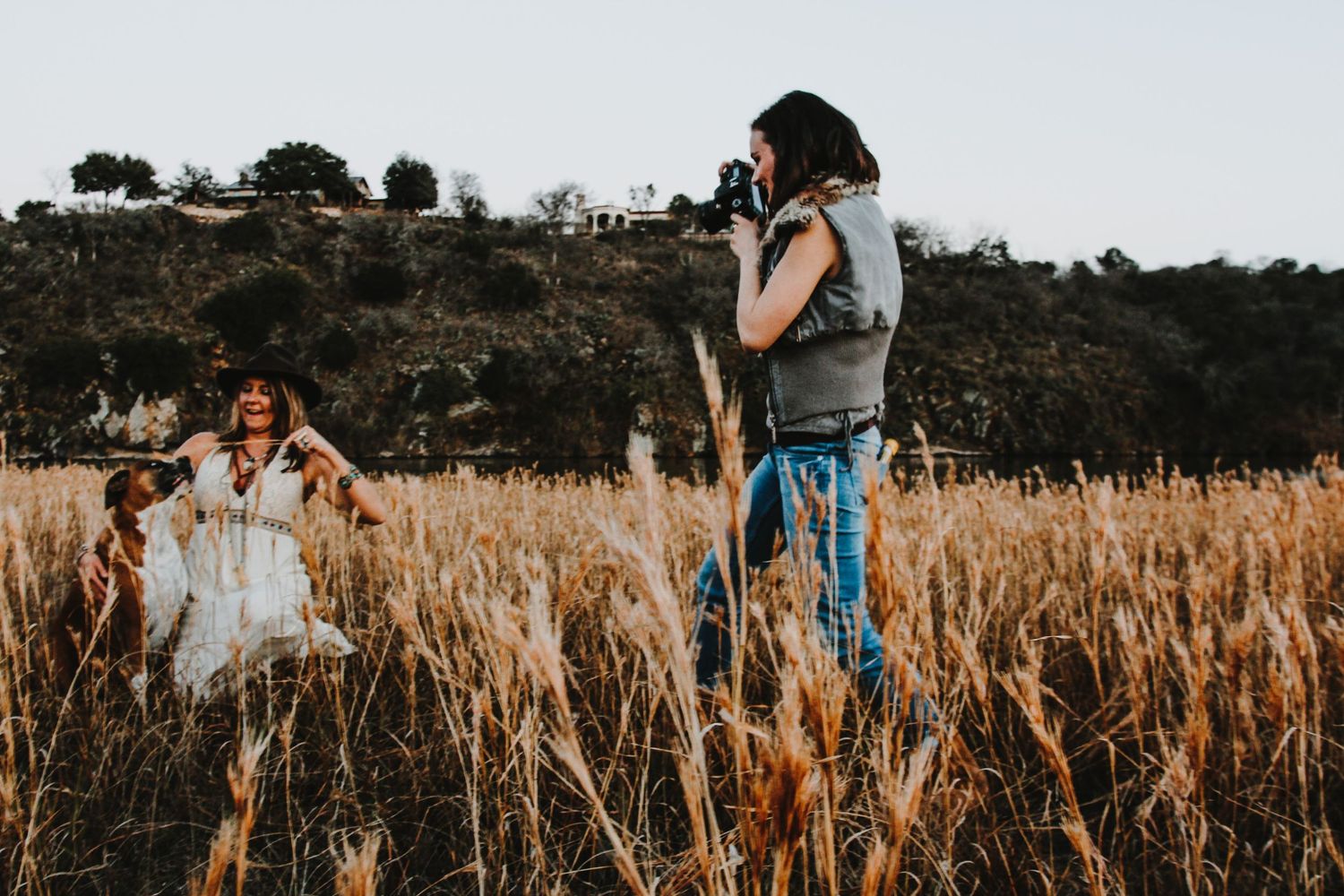 Photographer capturing a woman and her dog in a golden wheat field at sunset near Fallston MD in Harford County.