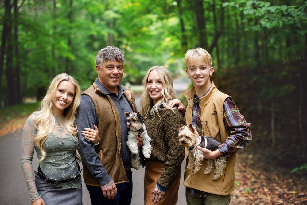 Family group photo in a wooded setting holding small pets while dressed in earth-toned casual clothing.