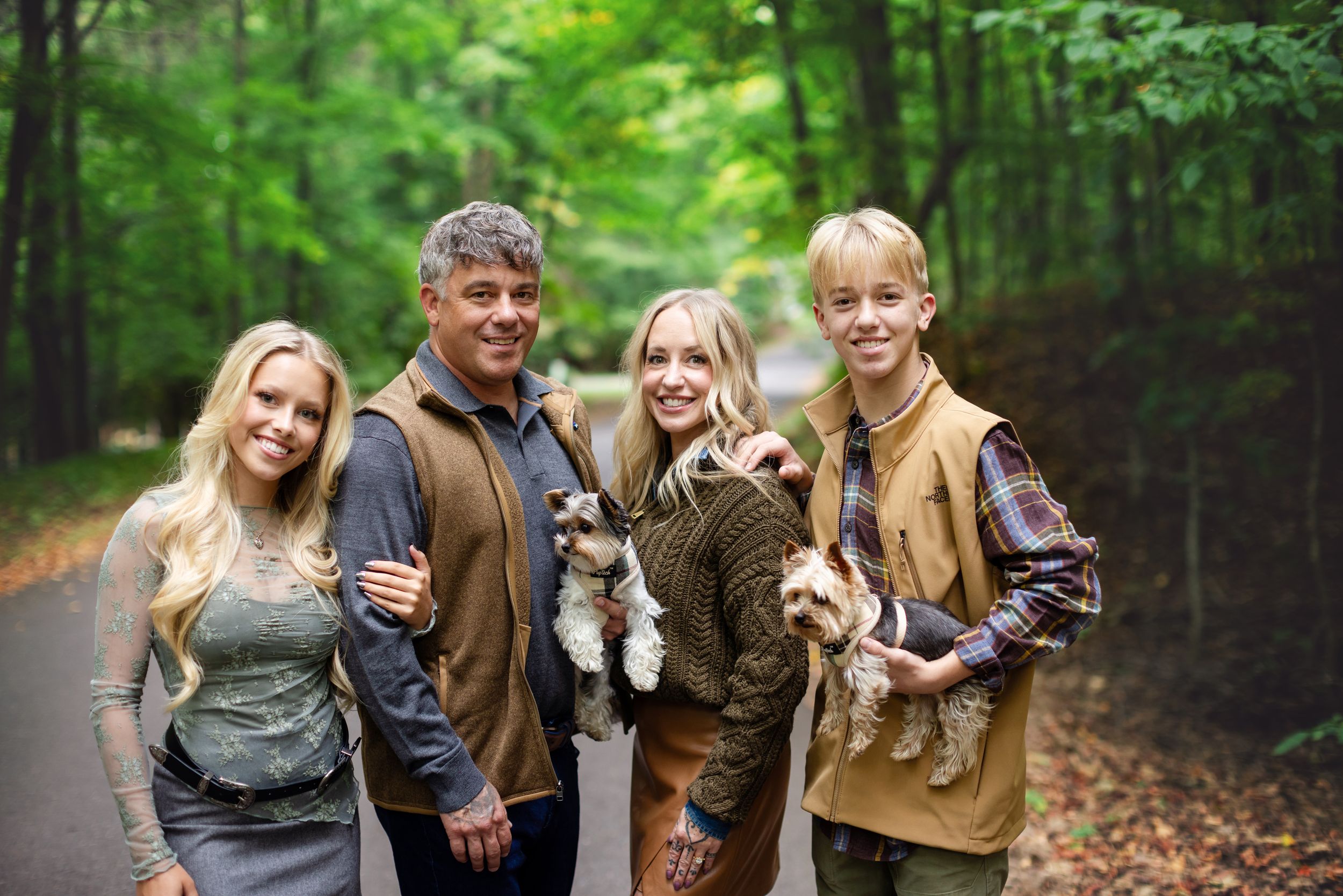 Family group photo in a wooded setting holding small pets while dressed in earth-toned casual clothing.