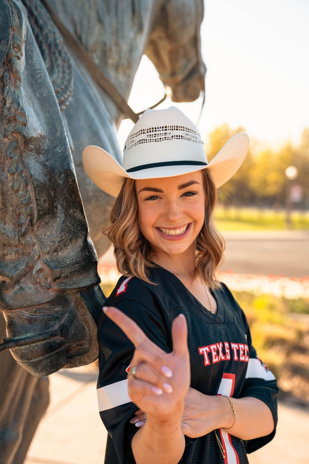 A Texas sports fan poses cheerfully by a horse statue in golden hour light.