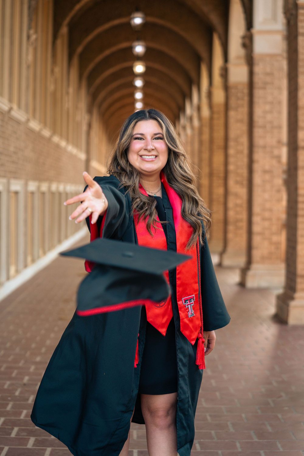 Graduate celebrates in cap and gown with Texas Tech stole in campus archway.