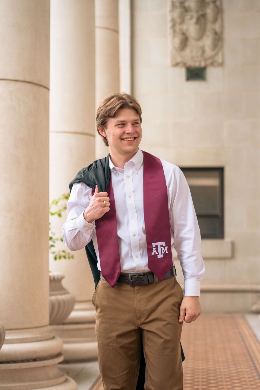 Graduate poses in formal attire with an A&M stole between classical columns.