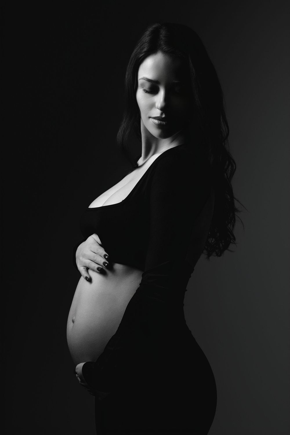 Dramatic black and white maternity portrait with side lighting.