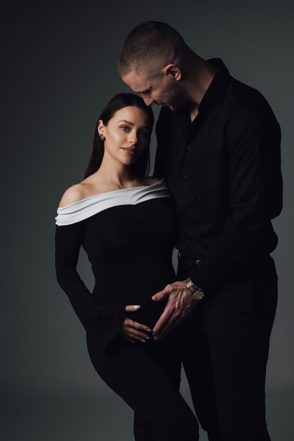 Couple in black clothing pose intimately against dark background.