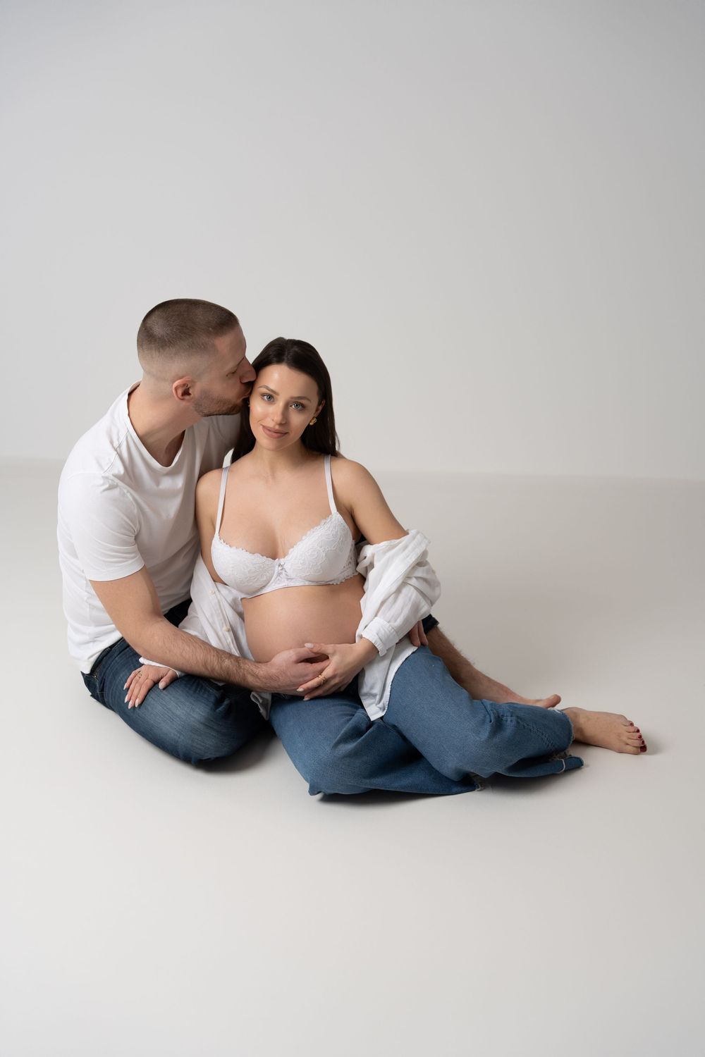 Intimate maternity portrait with couple in casual wear on light background.