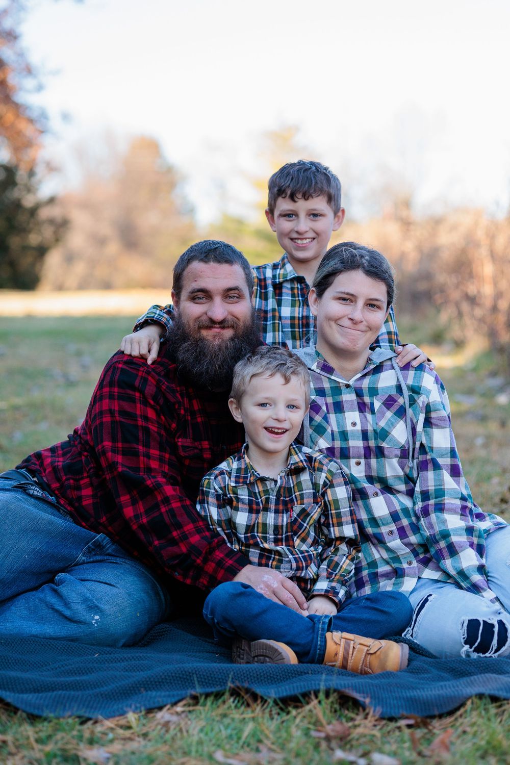 Family group relaxing on blue blanket outdoors during fall photo session.