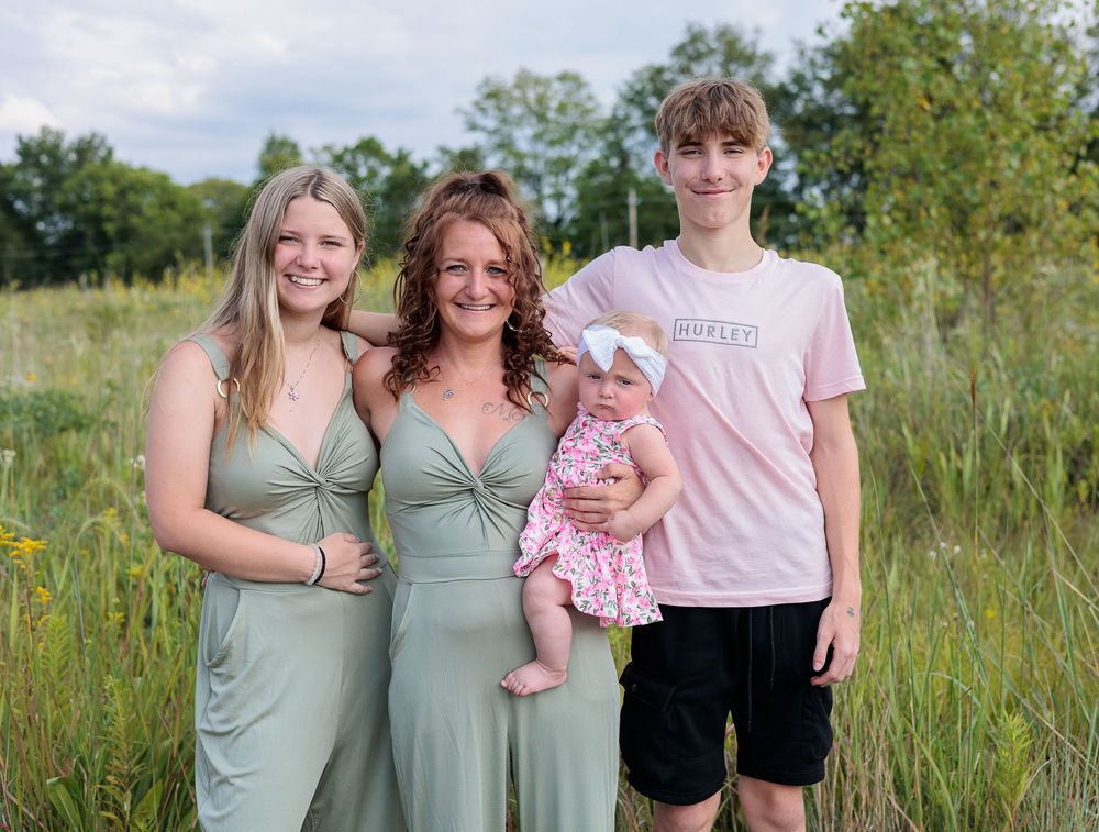 Group poses in sage green dresses and pink tops against natural field backdrop.