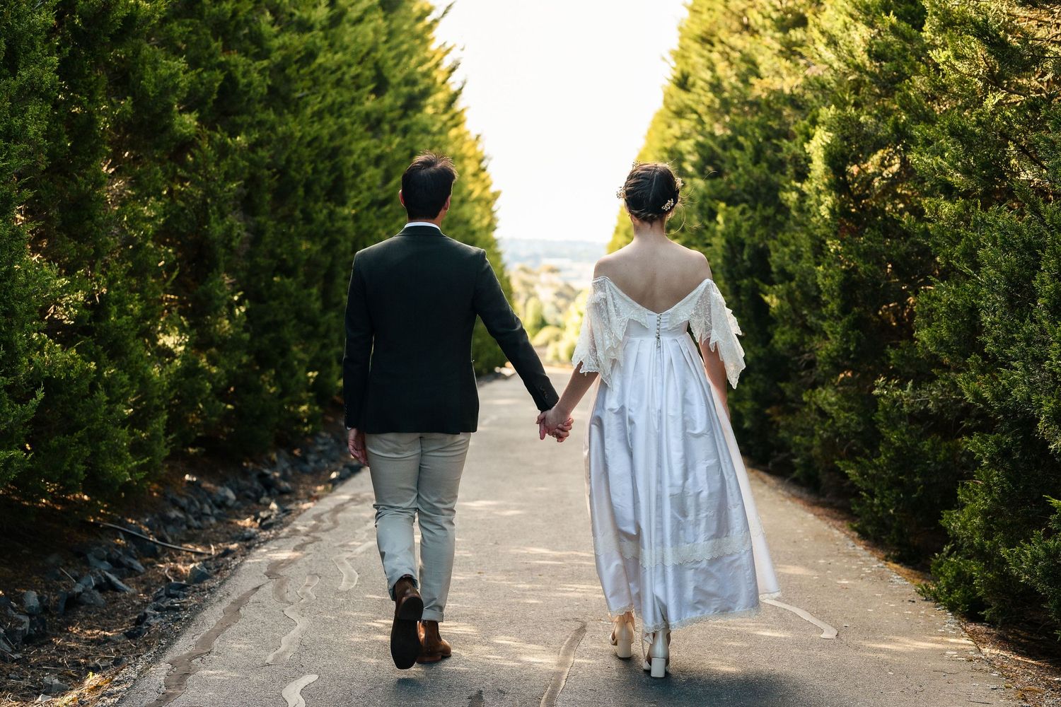 Back view of couple walking hand in hand down a tree-lined path during golden hour.