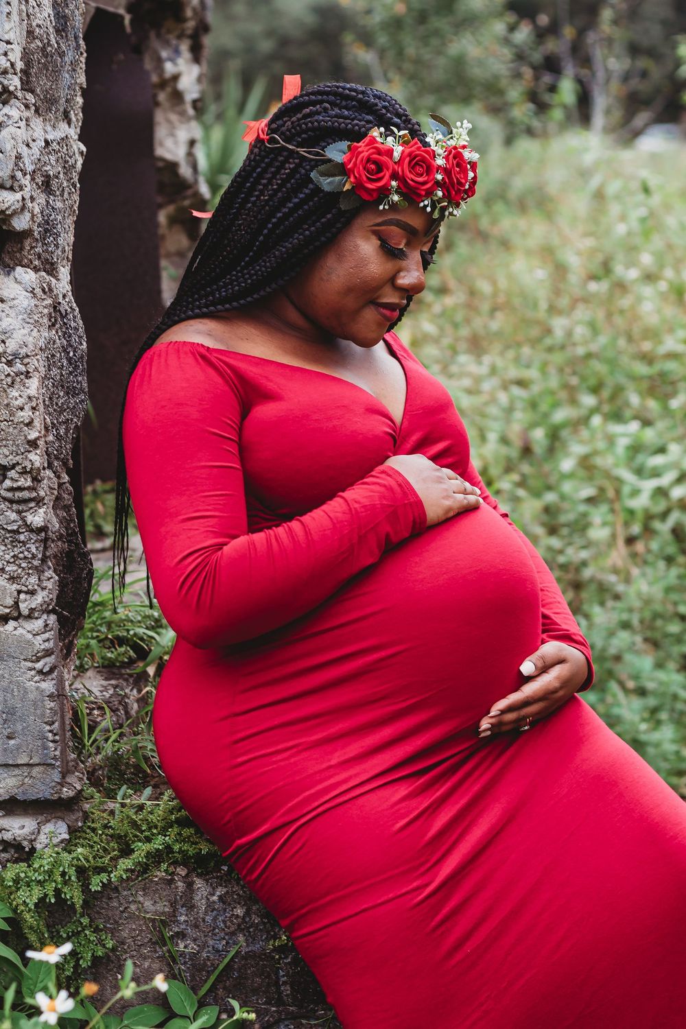 Pregnant woman in red dress with floral crown cradling baby bump outdoors at Riverbend Park Jupiter.