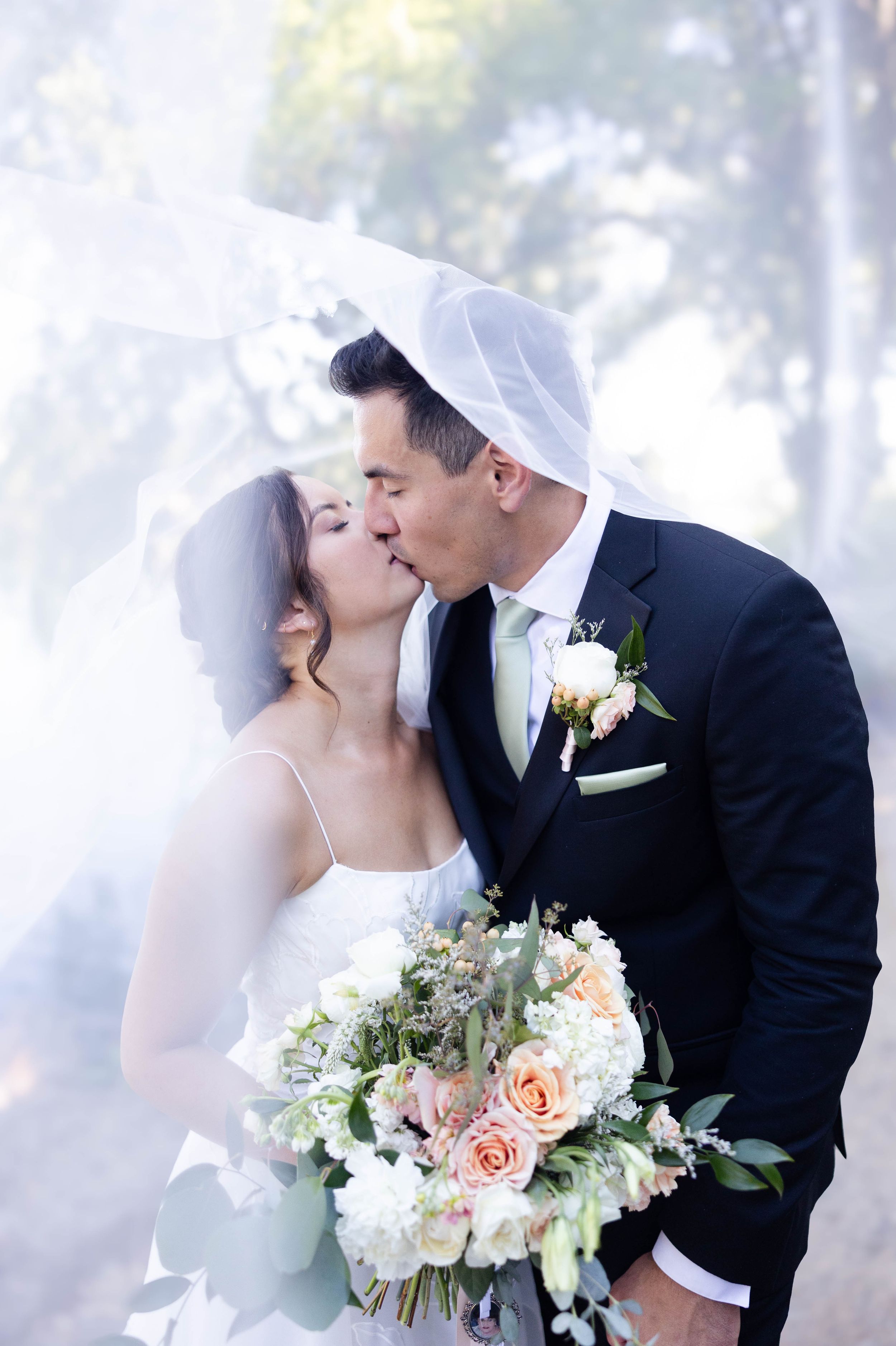 Bride and groom kissing under the veil during portraits after their wedding at lakeside pavilion in Chico, California