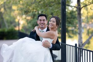 Bride holding groom on sidewalk with the lake behind them at lakeside pavilion in Chico, California