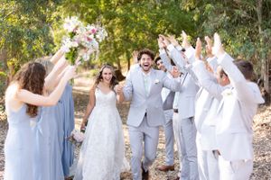 Bride and groom running through tunnel with wedding party with trees and pon in background in Orland, California Wedding