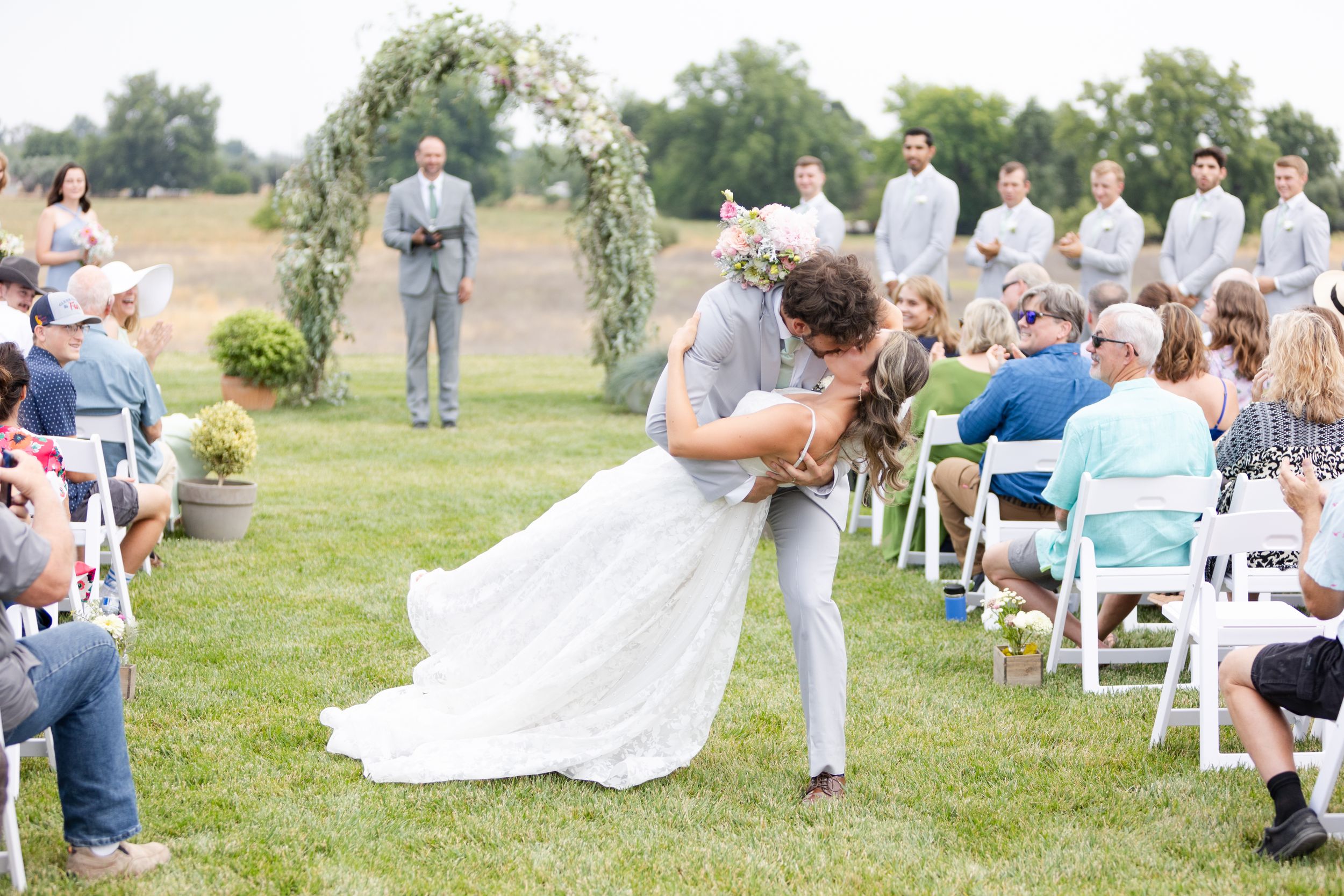 Groom dipping bride and kissing her during exit on beautiful lawn with pretty background in Orland, California Wedding.