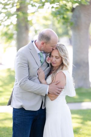 Groom kissing bride on lawn with green trees behind them immediately following the ceremony Orland, California Wedding