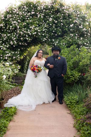 Bride and groom posing under a floral arch in a lush garden, bride holding colorful bouquet in white gown. White Ranch Venue, Chico Californ